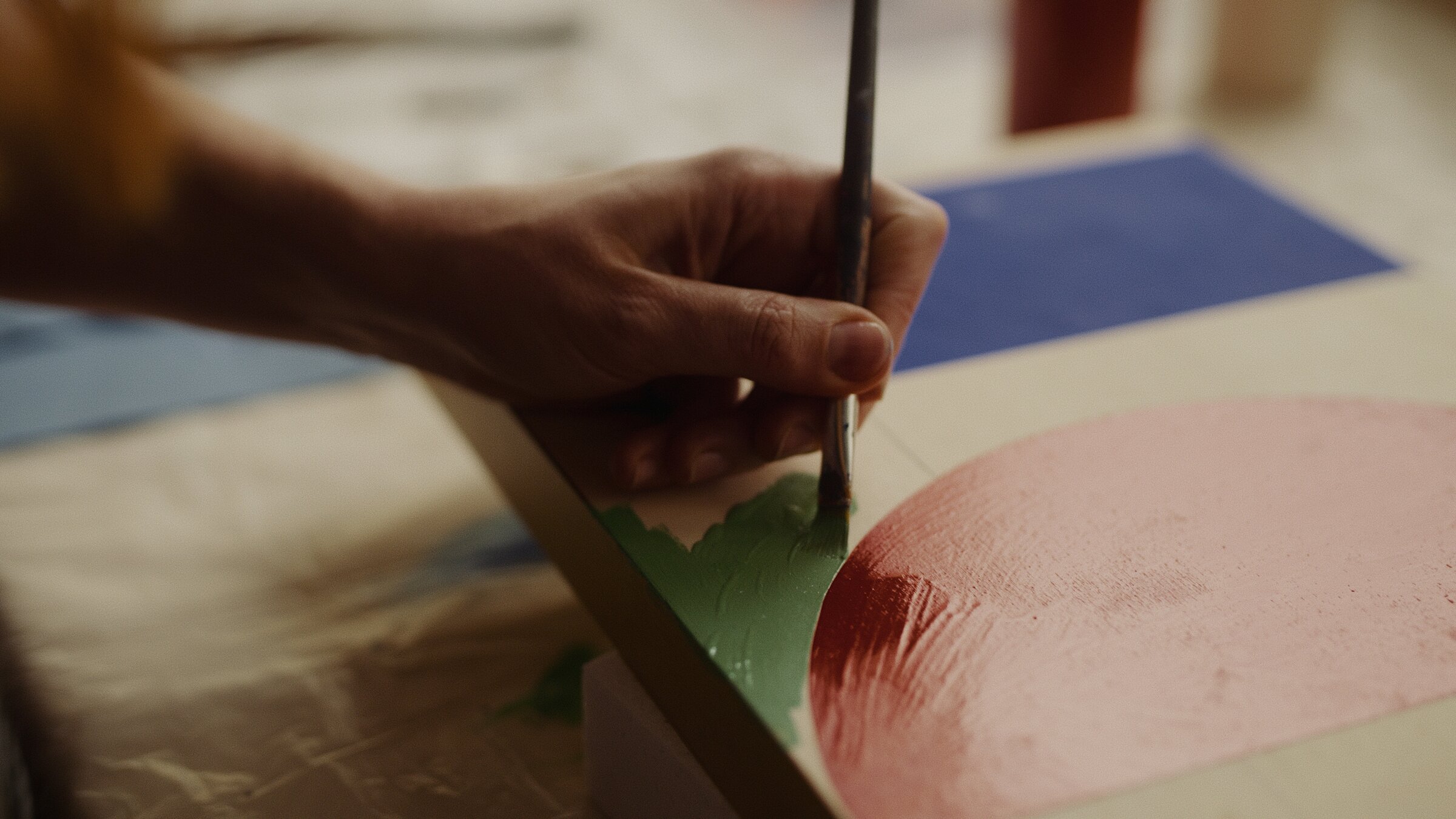 Close-up of a brush painting a curved red and green shape