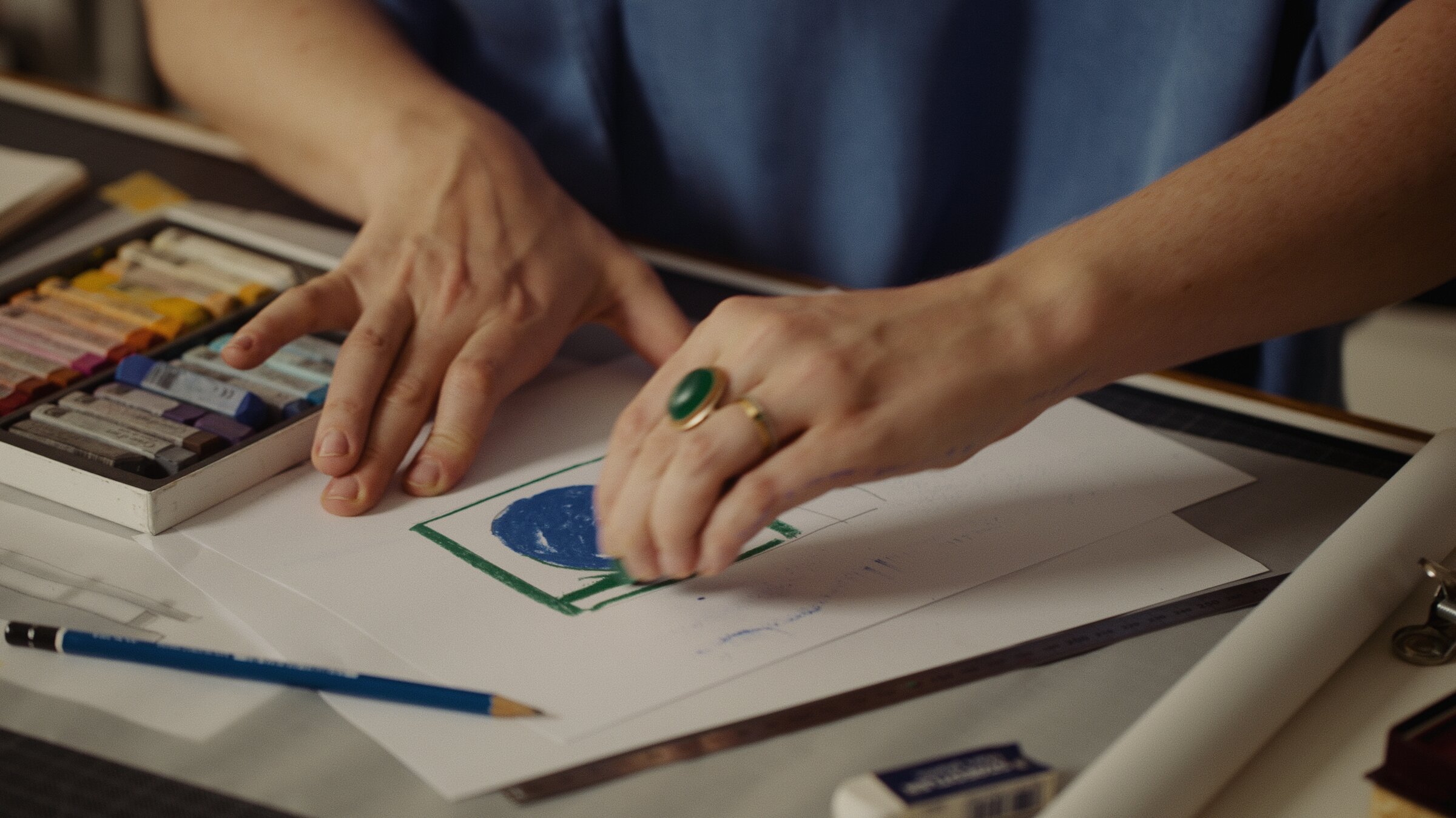 Hand wearing an emerald ring sketching a design in pastel