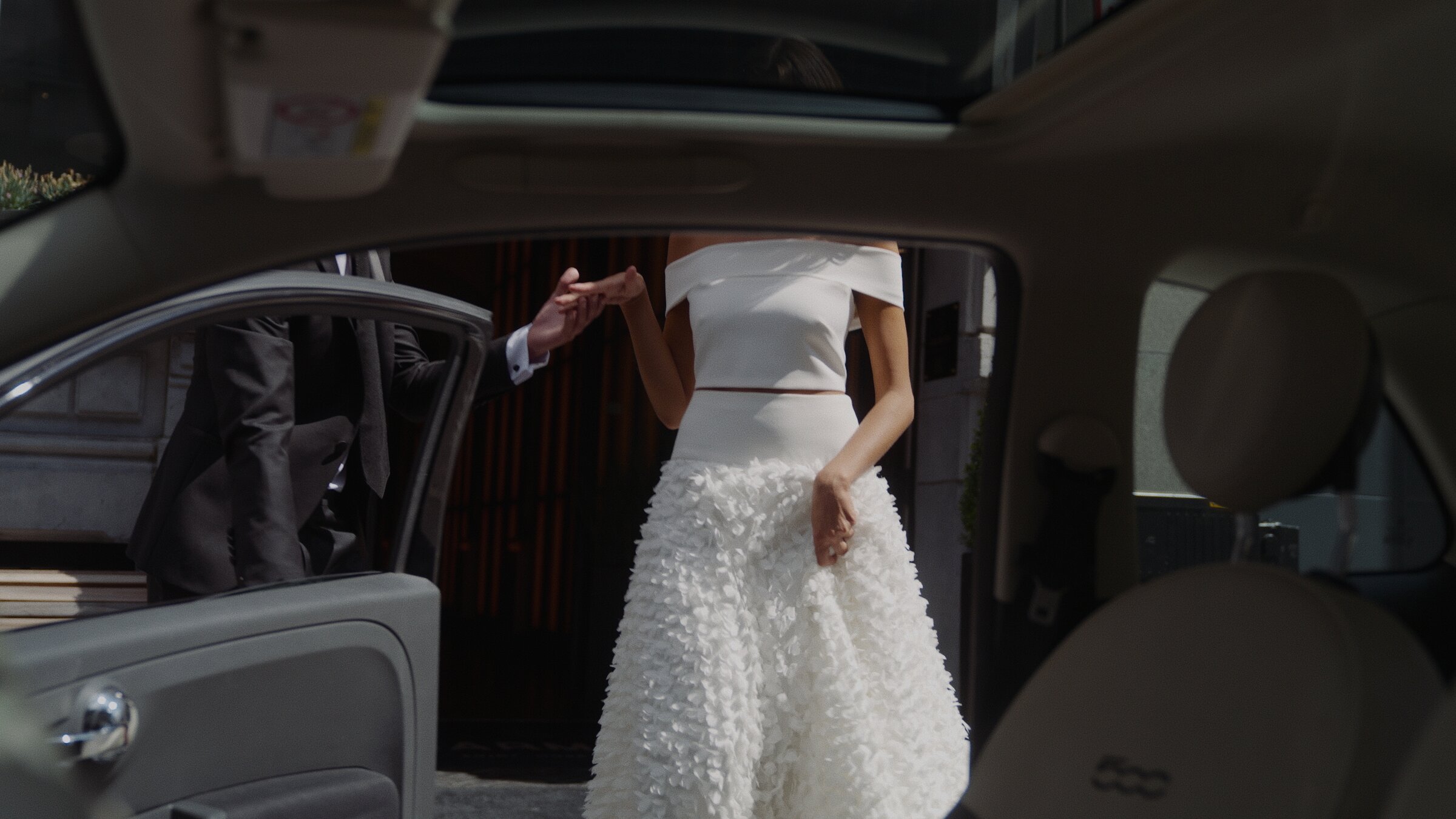 Bride in a textured white gown, hand held as she steps from a car