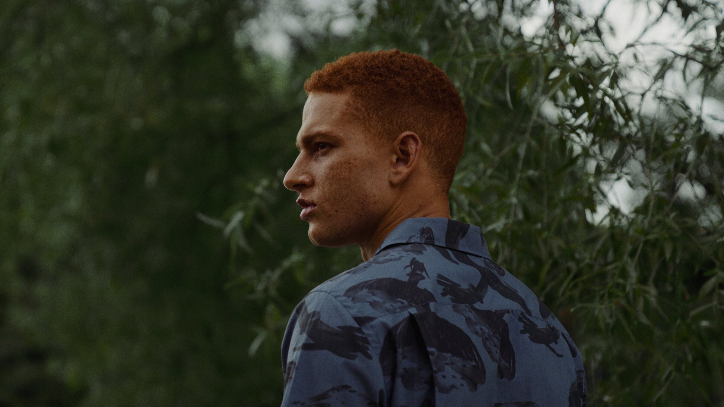 Male model portrait in a printed shirt, outdoor foliage backdrop