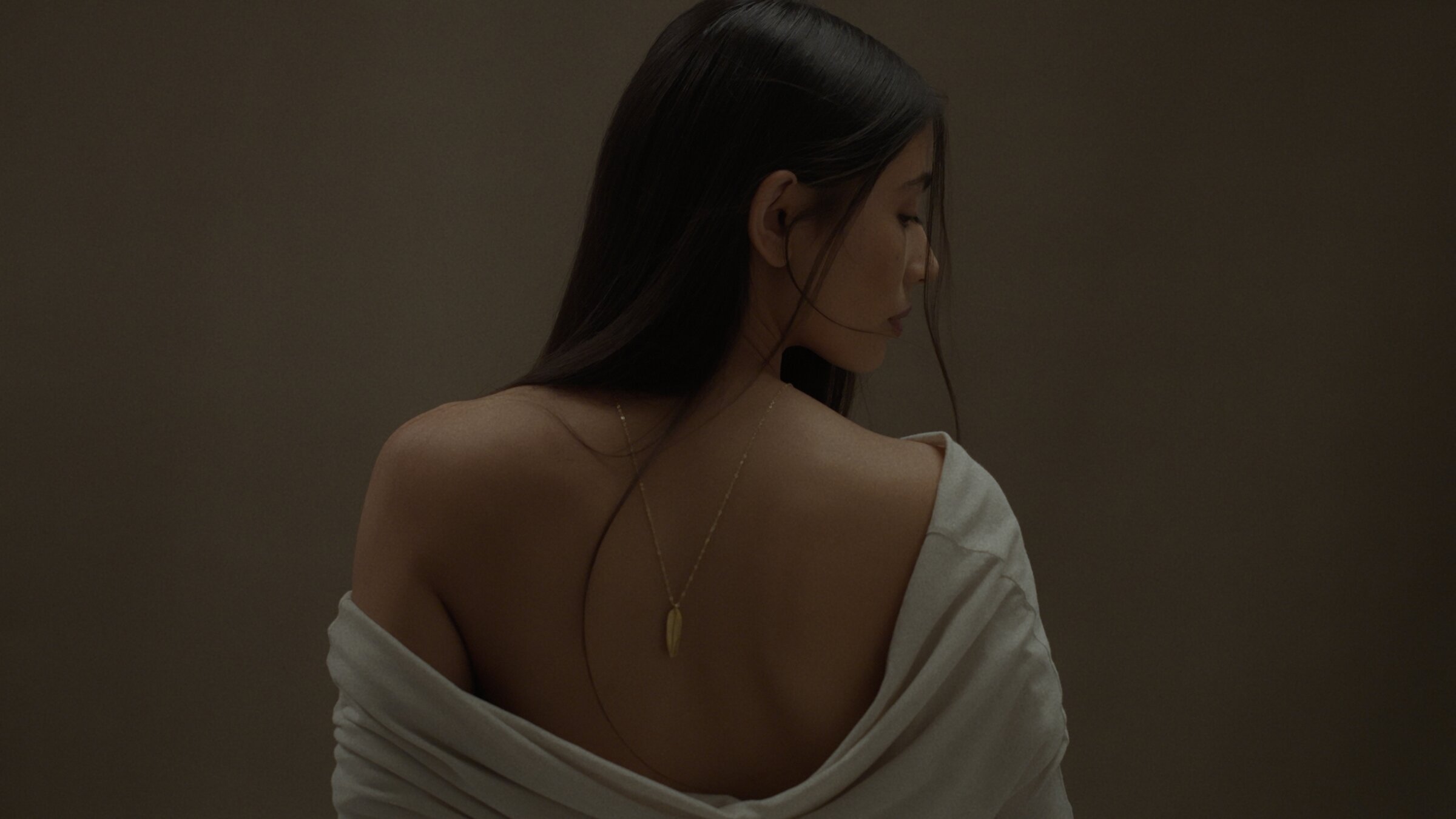 Studio portrait from behind, draped fabric and a gold pendant necklace