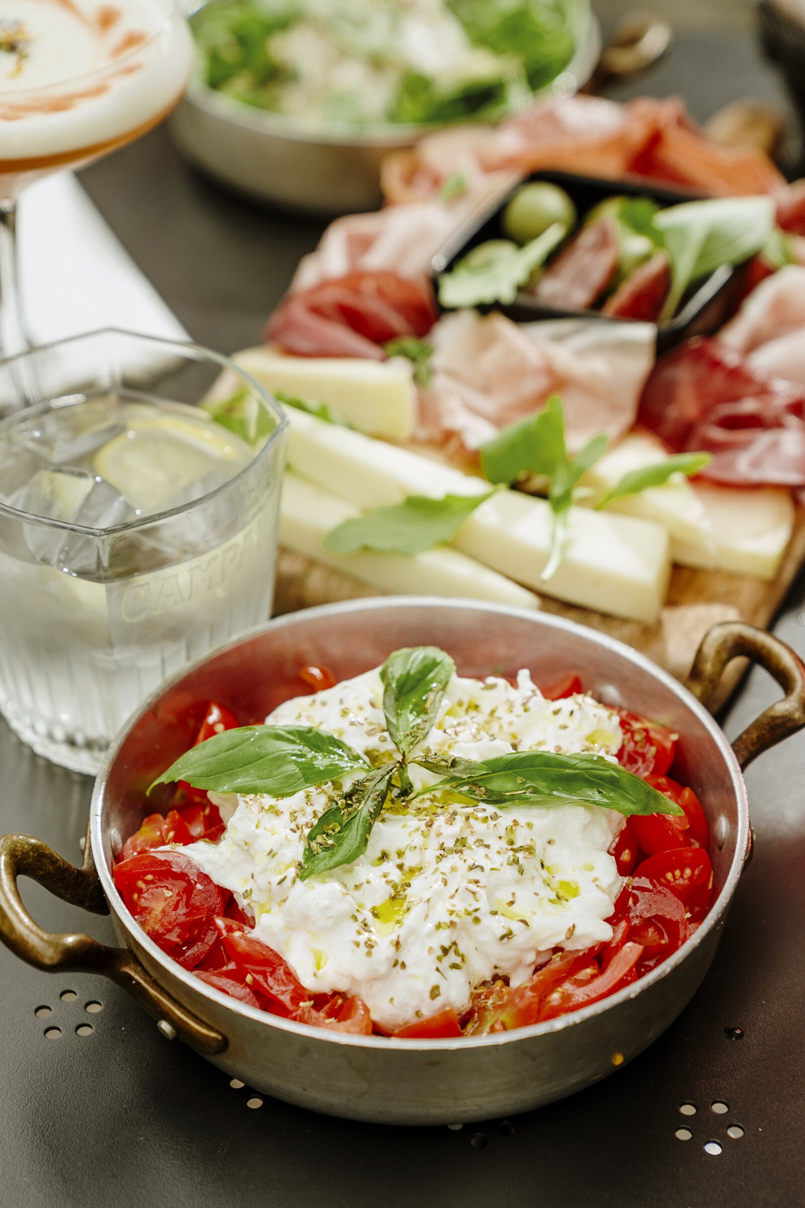 Burrata and tomato dish, charcuterie board and cocktail, restaurant table setting