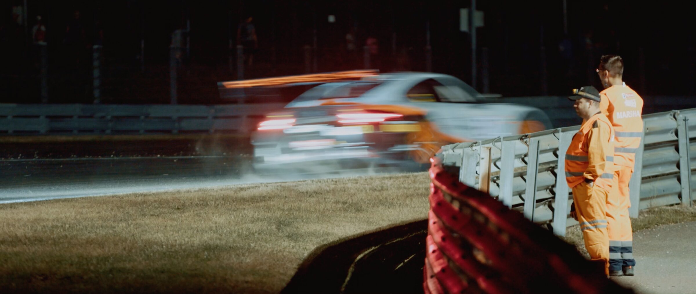 Marshals in orange watching a GT car blur past at night