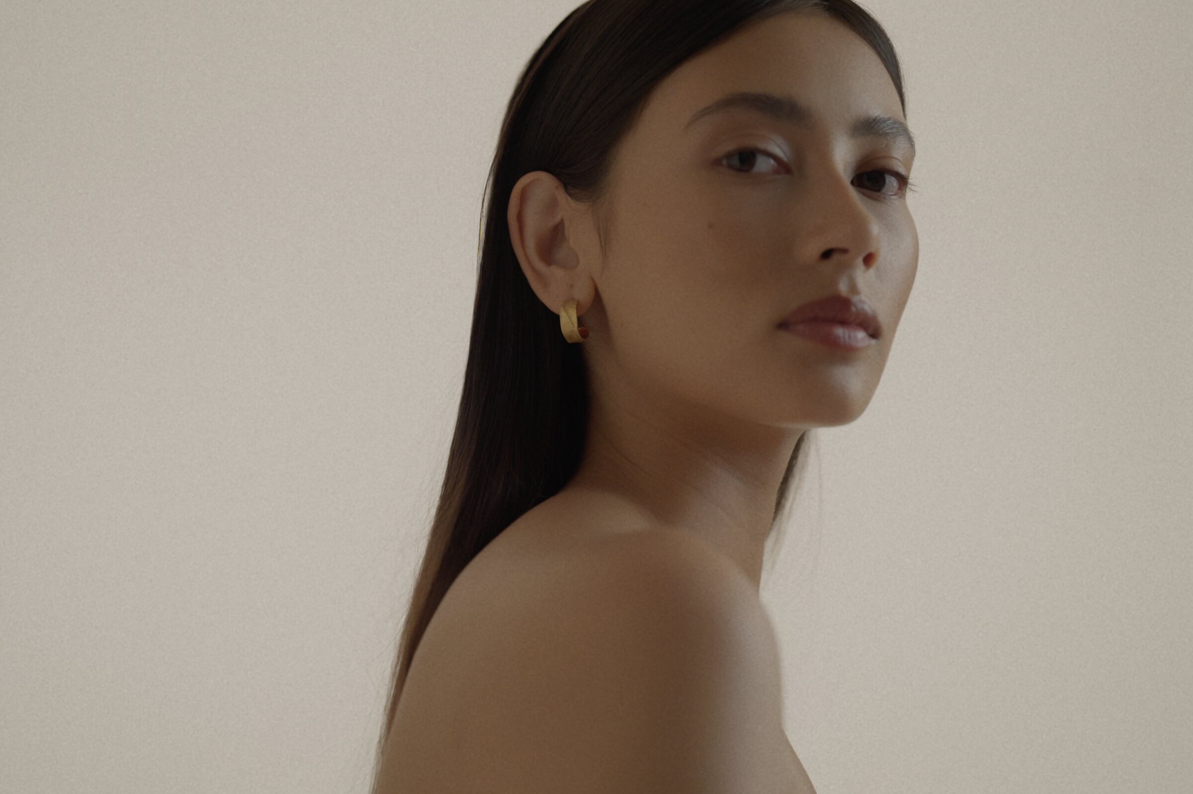 Side portrait, small gold hoop earring with a red bead accent, bare shoulder