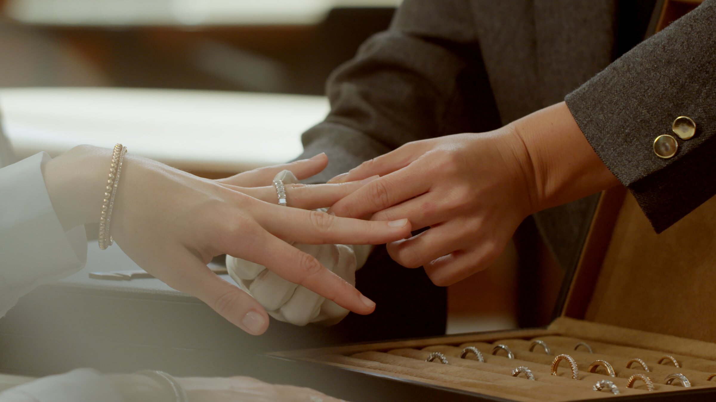 Two hands meeting over an open jewelry tray of diamond rings at the counter