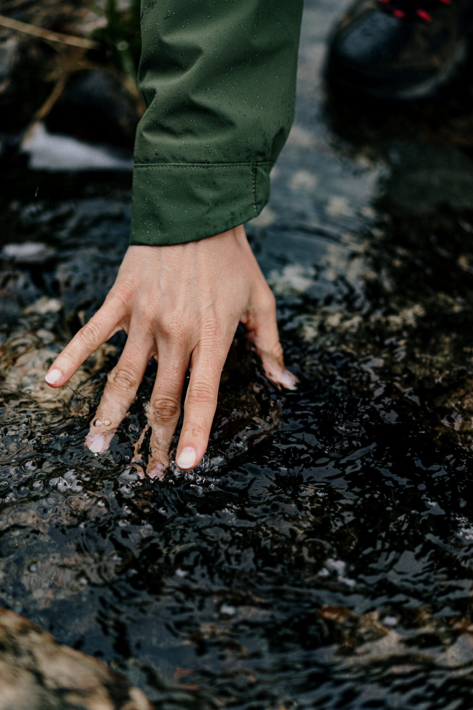 Hand trailing in a dark stream, hiking in the rain